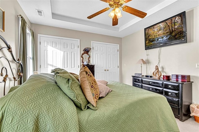 bedroom with a tray ceiling, ceiling fan, carpet, and two closets