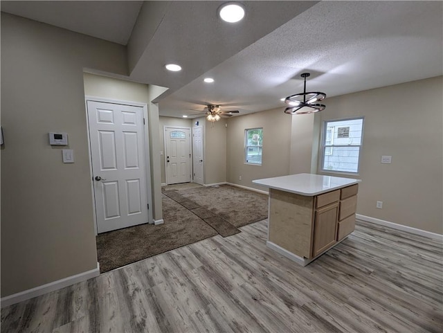 kitchen featuring light hardwood / wood-style floors, a textured ceiling, decorative light fixtures, a kitchen island, and ceiling fan with notable chandelier