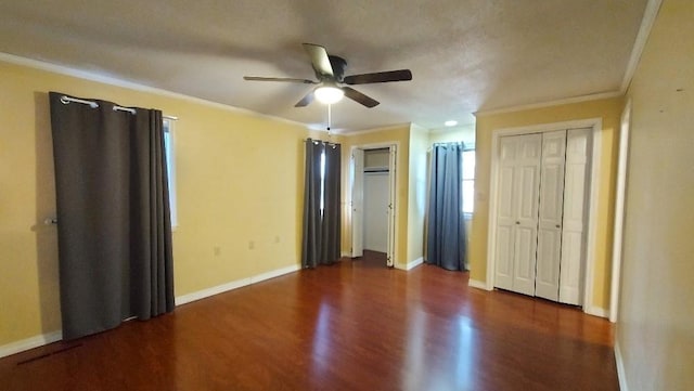 unfurnished bedroom with ceiling fan, dark wood-type flooring, a textured ceiling, two closets, and ornamental molding