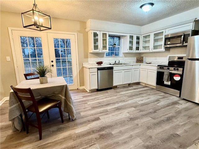 kitchen with light hardwood / wood-style flooring, appliances with stainless steel finishes, white cabinetry, a textured ceiling, and decorative light fixtures