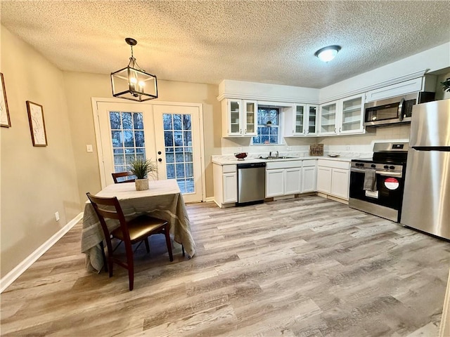 kitchen with sink, white cabinetry, light wood-type flooring, pendant lighting, and stainless steel appliances