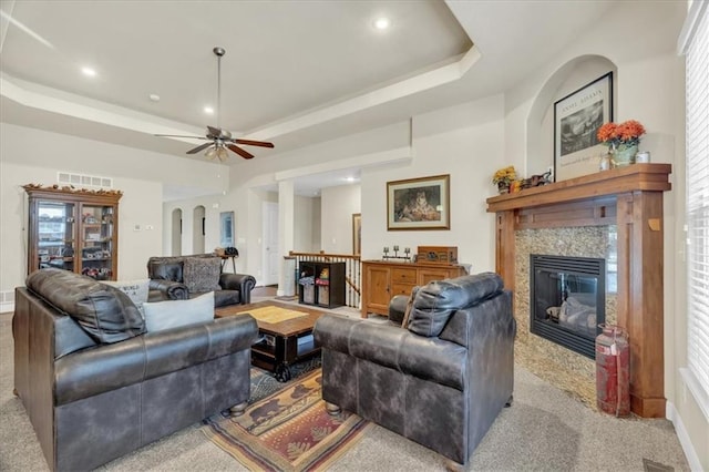 carpeted living room featuring a high end fireplace, a raised ceiling, and ceiling fan