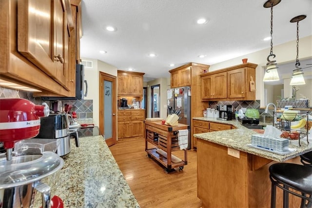 kitchen featuring decorative backsplash, light wood-type flooring, light stone counters, sink, and decorative light fixtures