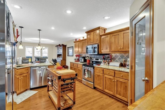 kitchen featuring stainless steel appliances, light stone counters, a chandelier, a textured ceiling, and light wood-type flooring