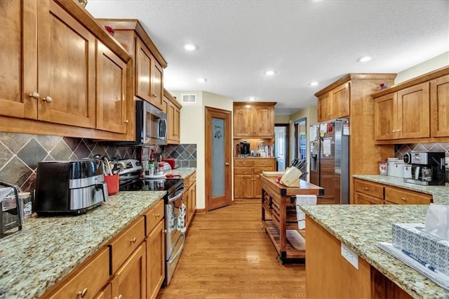 kitchen featuring tasteful backsplash, light stone countertops, stainless steel appliances, and light wood-type flooring