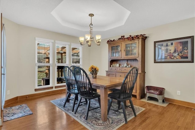 dining area featuring hardwood / wood-style flooring, an inviting chandelier, and a tray ceiling