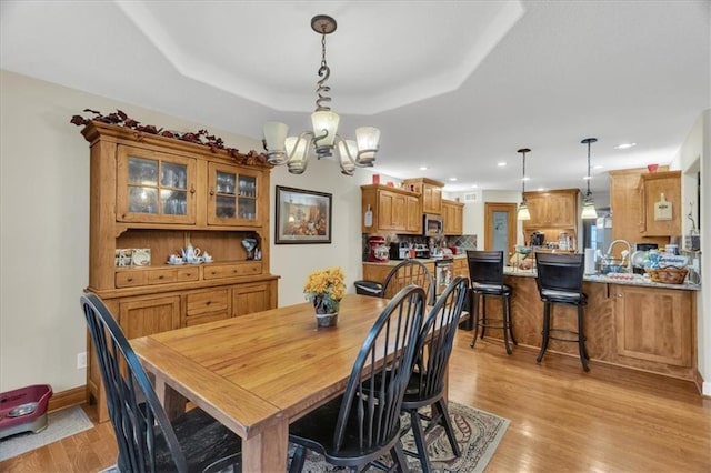 dining space with a raised ceiling, light hardwood / wood-style floors, and an inviting chandelier