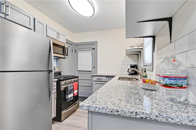 kitchen featuring light stone countertops, sink, light wood-type flooring, and stainless steel appliances