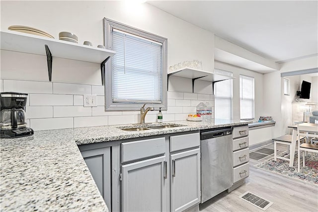 kitchen featuring dishwasher, sink, light wood-type flooring, light stone countertops, and tasteful backsplash