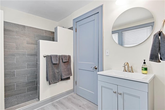 bathroom featuring a tile shower, vanity, and wood-type flooring