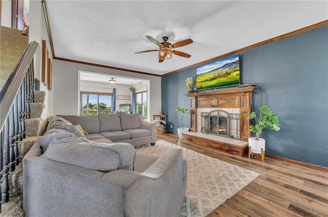 living room featuring hardwood / wood-style flooring, ceiling fan, crown molding, and a textured ceiling