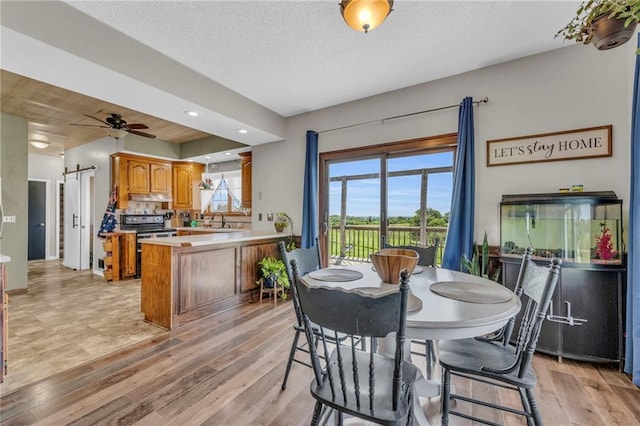 dining area featuring a barn door, ceiling fan, light hardwood / wood-style flooring, and a textured ceiling