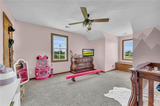 bedroom featuring ceiling fan, light colored carpet, a textured ceiling, and a nursery area