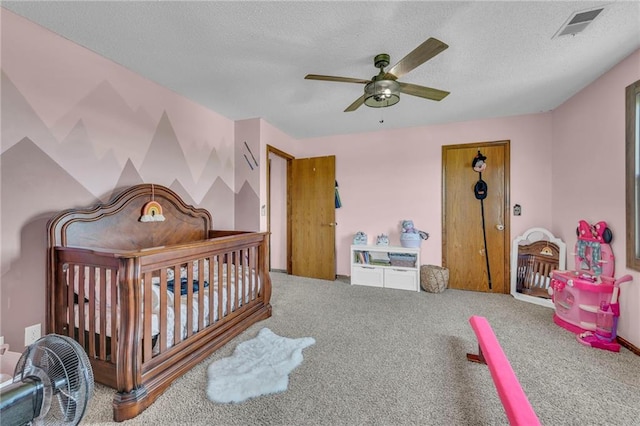 carpeted bedroom with a textured ceiling, a nursery area, and ceiling fan