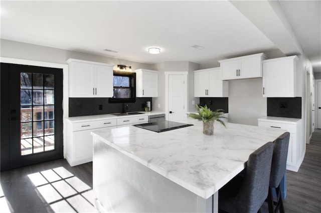 kitchen featuring white cabinets, a kitchen island, dark wood-type flooring, and light stone counters