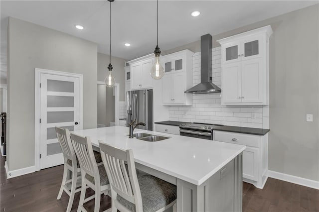 kitchen with a sink, wall chimney range hood, appliances with stainless steel finishes, glass insert cabinets, and pendant lighting