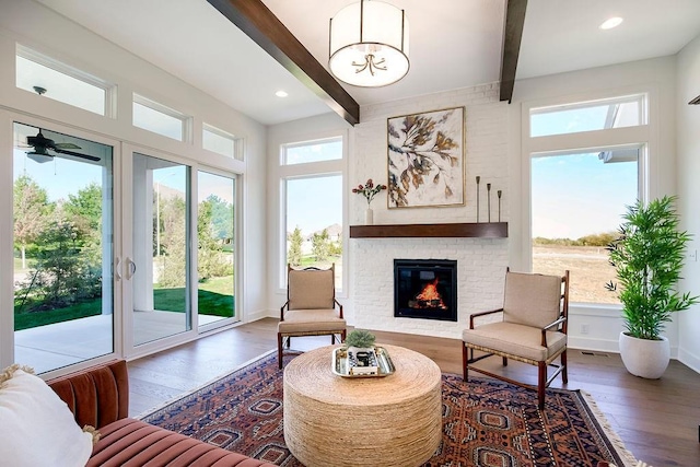 sitting room with beamed ceiling, a fireplace, dark wood-type flooring, and ceiling fan with notable chandelier