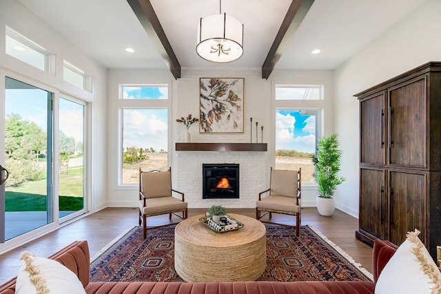 sitting room with beam ceiling, an inviting chandelier, dark wood-type flooring, and a brick fireplace