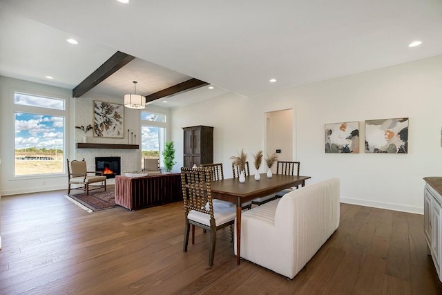 dining area featuring beam ceiling, a wealth of natural light, a fireplace, and dark wood-type flooring