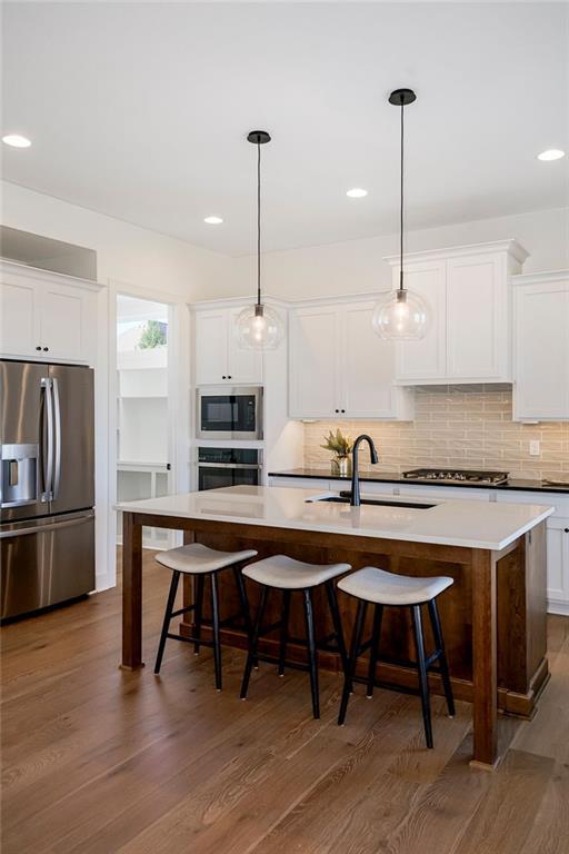 kitchen featuring appliances with stainless steel finishes, sink, pendant lighting, a center island with sink, and white cabinetry