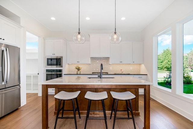 kitchen featuring sink, hanging light fixtures, an island with sink, white cabinetry, and stainless steel appliances