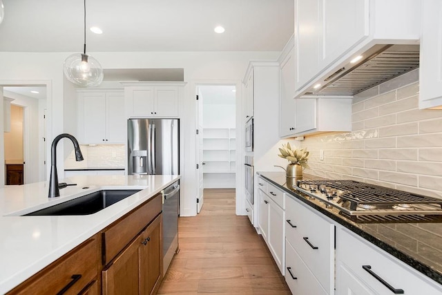 kitchen featuring wall chimney exhaust hood, stainless steel appliances, sink, white cabinets, and hanging light fixtures