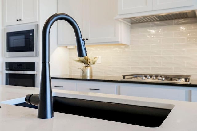 kitchen featuring tasteful backsplash, built in microwave, exhaust hood, white cabinetry, and oven