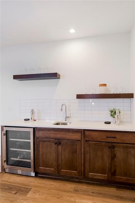 bar featuring sink, wine cooler, light hardwood / wood-style flooring, decorative backsplash, and dark brown cabinetry