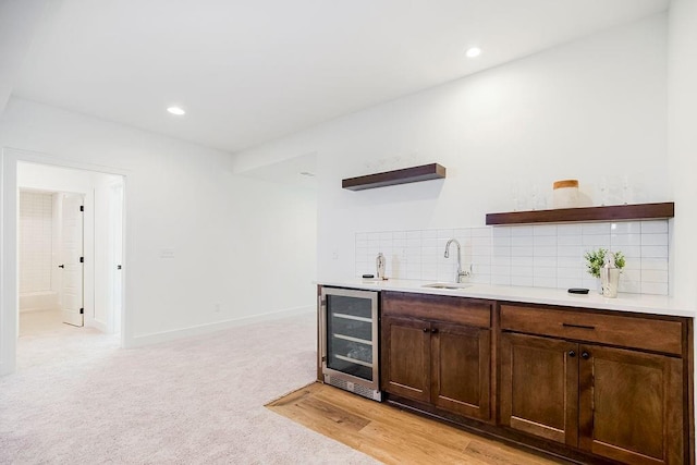 bar with light carpet, backsplash, dark brown cabinetry, beverage cooler, and sink