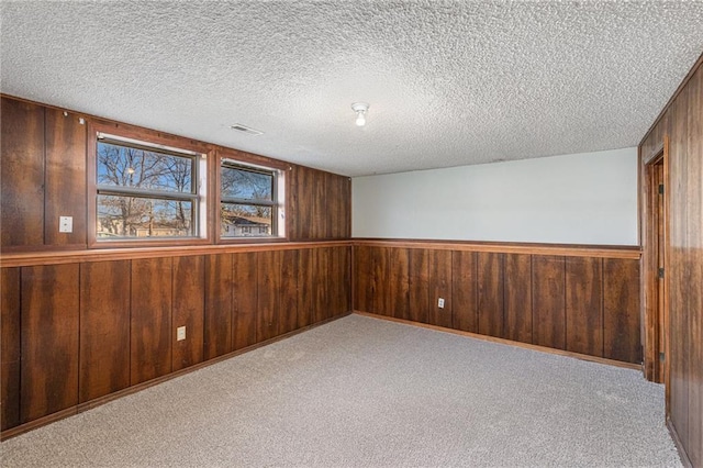 empty room with a textured ceiling, light colored carpet, and wooden walls