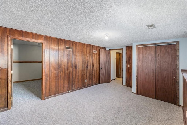 unfurnished bedroom featuring a textured ceiling, wooden walls, and light carpet