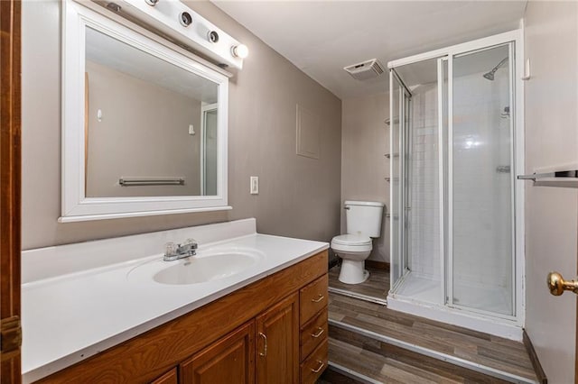 bathroom featuring wood-type flooring, vanity, toilet, and a shower with shower door