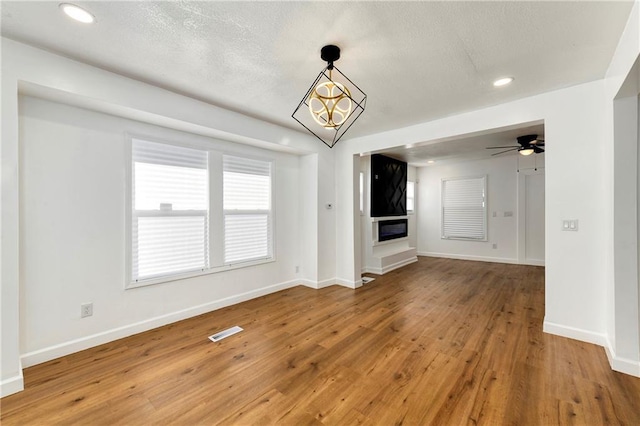 unfurnished living room with ceiling fan with notable chandelier and hardwood / wood-style flooring