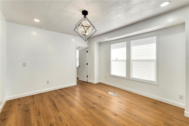 empty room featuring hardwood / wood-style flooring, a textured ceiling, and a chandelier