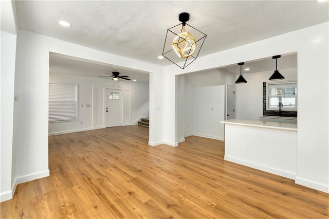 unfurnished living room featuring ceiling fan with notable chandelier and light hardwood / wood-style flooring