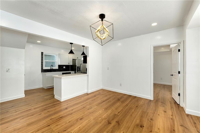 kitchen featuring decorative light fixtures, white cabinetry, light hardwood / wood-style floors, backsplash, and stainless steel fridge with ice dispenser