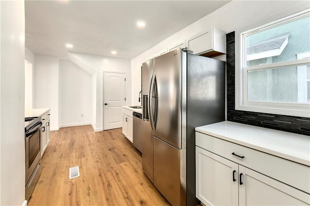 kitchen with stainless steel appliances, light wood-type flooring, sink, white cabinetry, and tasteful backsplash