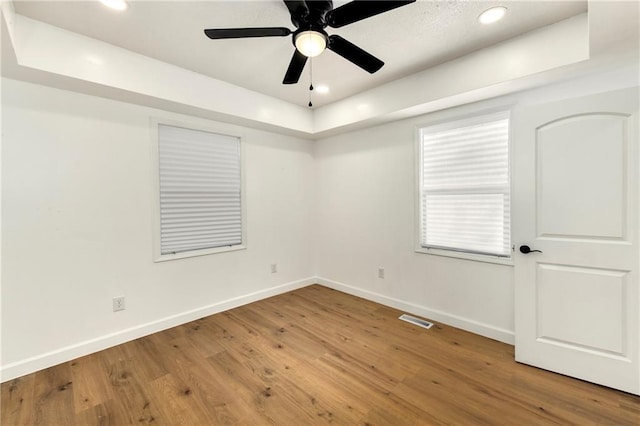 empty room with ceiling fan, hardwood / wood-style flooring, and a tray ceiling