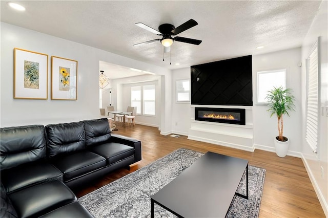 living room with a large fireplace, ceiling fan, hardwood / wood-style floors, and a textured ceiling