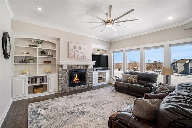 living room with a stone fireplace, ceiling fan, dark hardwood / wood-style floors, built in features, and ornamental molding