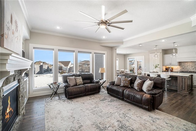 living room featuring ceiling fan, dark wood-type flooring, ornamental molding, and a stone fireplace