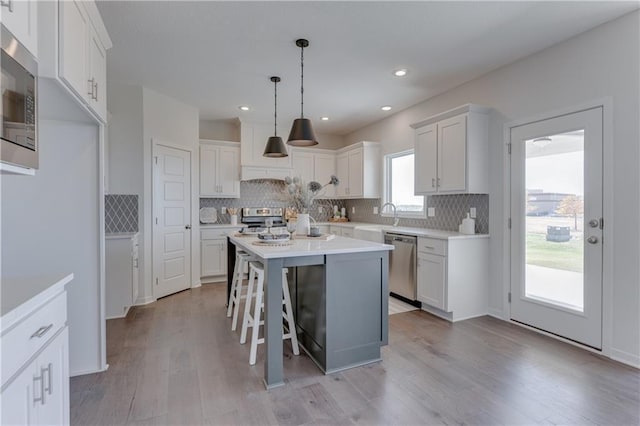 kitchen with white cabinets, a kitchen breakfast bar, hanging light fixtures, a center island, and stainless steel appliances