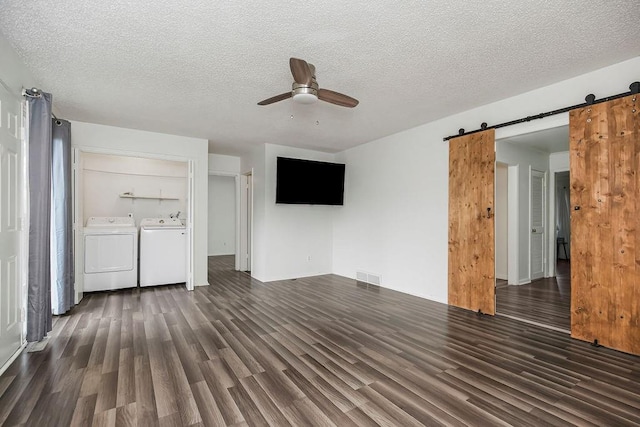 unfurnished living room featuring a barn door, ceiling fan, a textured ceiling, and independent washer and dryer