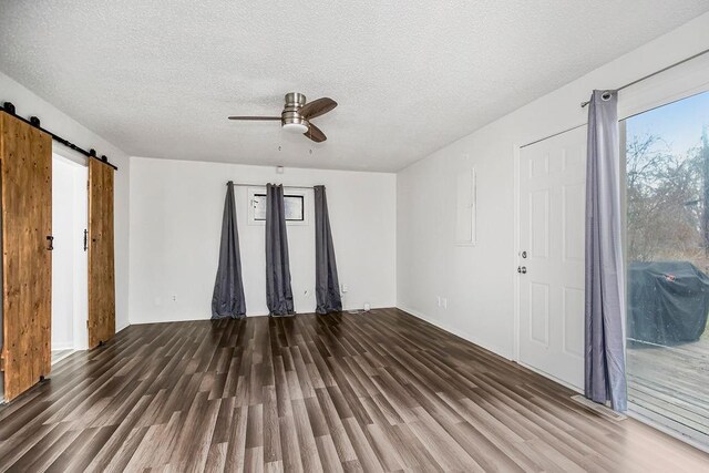 unfurnished room featuring ceiling fan, a barn door, dark hardwood / wood-style floors, and a textured ceiling