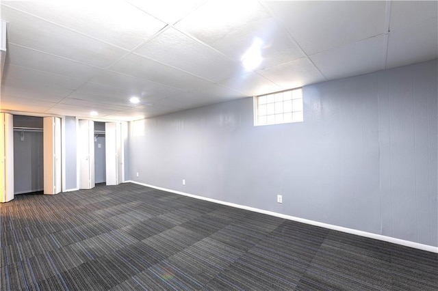 basement featuring a paneled ceiling and dark carpet