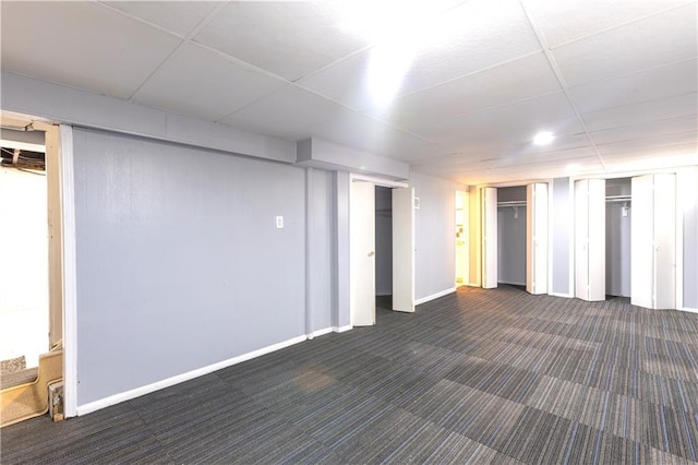 basement featuring dark colored carpet and a paneled ceiling