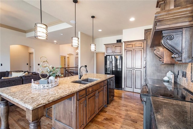 kitchen with a kitchen bar, sink, black refrigerator with ice dispenser, a center island with sink, and dark stone countertops