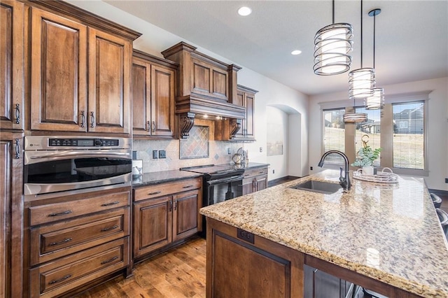 kitchen featuring hanging light fixtures, sink, oven, and light stone counters