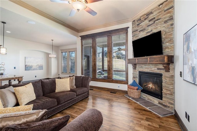 living room with wood-type flooring, a stone fireplace, ceiling fan, and crown molding