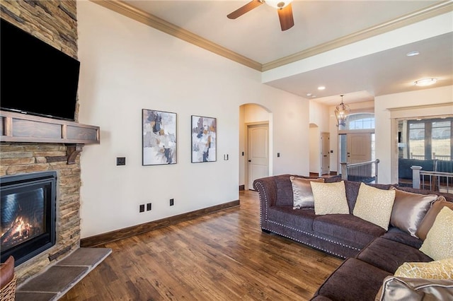 living room featuring ornamental molding, a stone fireplace, dark wood-type flooring, and ceiling fan